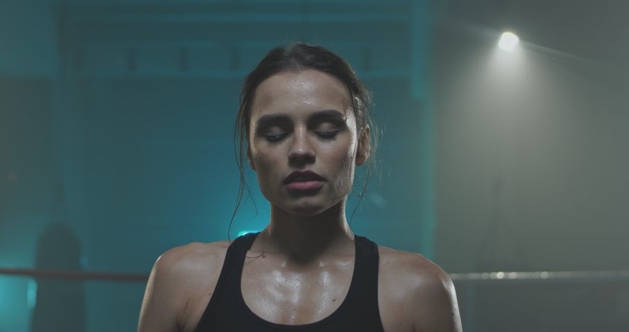 Close up of Caucasian young tired sweaty woman in sportswear standing in fron of camera and wiping her forehead with hand. Boxing training concept. Spotswoman after working out.
