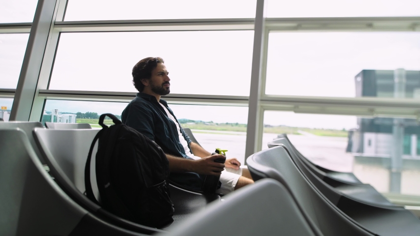 The young, handsome man sitting alone at the airport in a waiting room. A handsome guy is looking at his passport and ticket. Positive tourist at the airport before a flight.