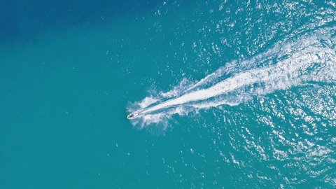 Aerial view Over Small Speed Boat in the bay during sunset. Drone Shot of Young Woman riding on Boat Rushing Toward in Exotic Scenic Seascape. Water sport top view. Amazing Aerial view of Tropical