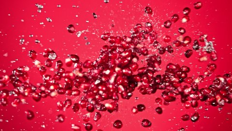 Super Slow Motion Shot of Fresh Pomegranate Seeds and Water Side Collision on Red Background at 1000fps.