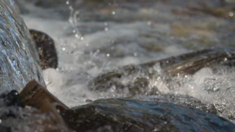 Close up of crystal clear waterfall splashing onto rocks in a stream slow motion