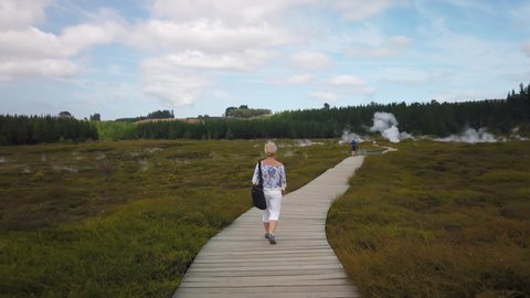 4k forward tracking motion of woman walking the boardwalk through the geothermal landscape of The Craters of The Moon Geothermal Walking trail, Taupo,North Island,New Zealand