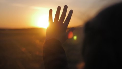 Girl looks at the sun through her hand at sunset.