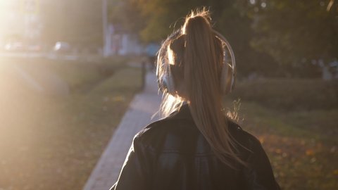 Young girl in headphones listening to music and sings favorite songs in the autumn city park. The girl is in a great mood and happy. Happy childhood.