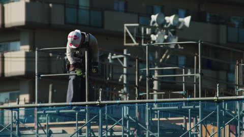 Construction worker on a building site in Japan. He is working with a spanner on scaffolding and is wearing a hard hat