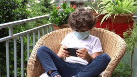 Italy , Milan  - white children boy six years old looking and playing with smartphone internet technology during covid19 Coronavirus quarantine home lockdown -  Child playing video game at balcony