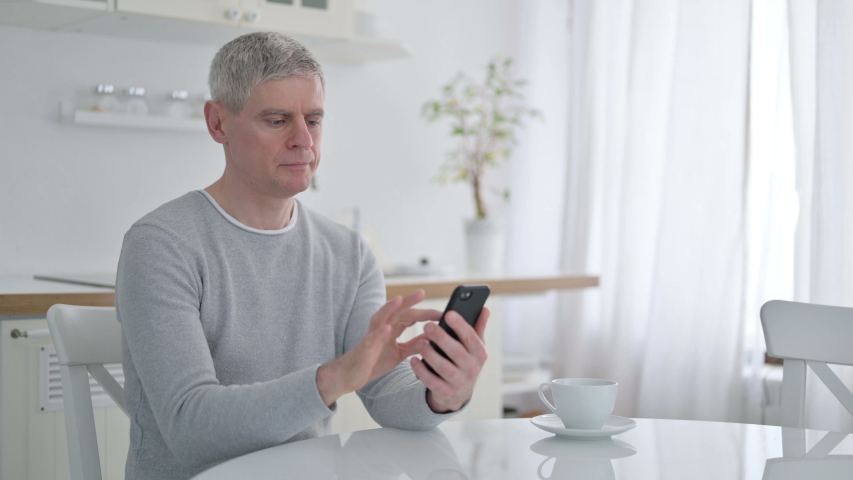 Senior Old Man Celebrating Success on Smartphone at Home 