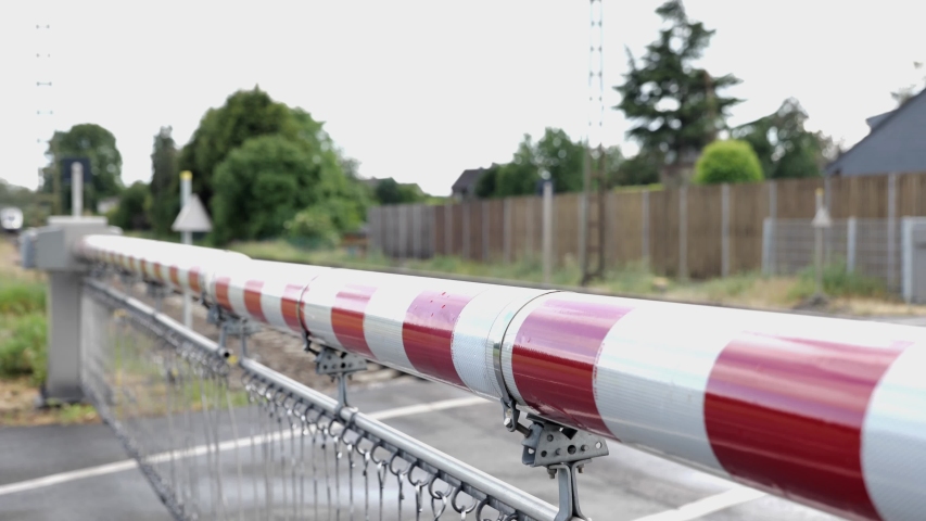 Selected focus view at red and white level crossing railway barrier which block the road until it was lifted, blur background of locomotive move on the rail on countryside. Royalty-Free Stock Footage #1054201319