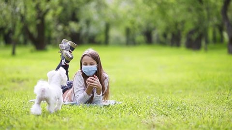 Little girl wearing a protective mask with white dog outdoors because of the coronavirus pandemic