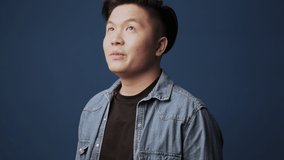 An excited young asian man wearing casual clothes is looking at something inspiring isolated over dark blue wall background in studio
