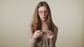 Young displeased woman isolated over grey wall background watch videos by mobile phone