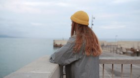 Portrait from behind of young beautiful millenial hipster girl on the seaside with water on the background, pure blue sky, enjoy of vacation and traveling