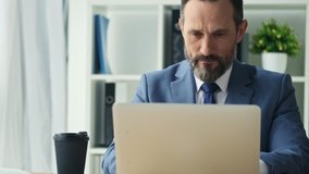 Focused mature man is working with his laptop computer in office