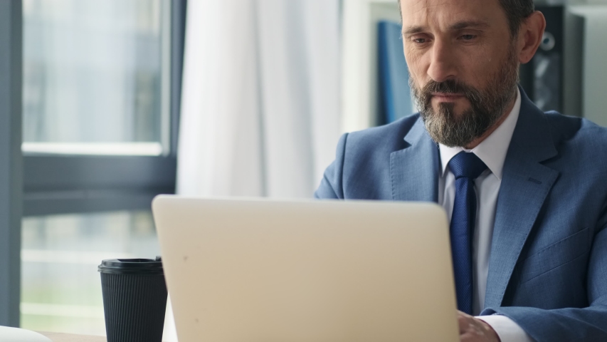 A serious mature man is working with his laptop computer in office Royalty-Free Stock Footage #1054208843