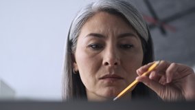 A close-up view of a thoughtful mature woman is looking to her laptop while working in the office