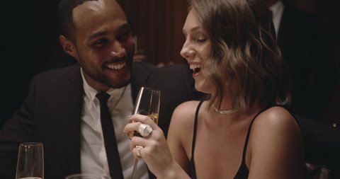 Man whispering something funny to a woman at dinner. Couple enjoying together at gala party, smiling and toasting wine.
