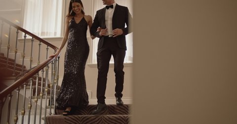 Beautiful couple walking down the stairs. Woman in evening gown and man in tuxedo moving down the staircase hand in hand.

