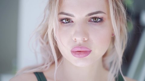 Portrait of close up of young sexy sporty blonde girl. Athlete with green eye makeup and pink lipstick on her lips. Sexually bites his lips. He poses and looks at the camera. Female is a fitness