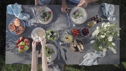 Family dinner outdoors. Aerial view or top view. Family dinner with organic salad and cheese on trendy scandinavian style table in garden. Healthy aesthetic beautiful food, summer staycation concept ஸ்டாக் வீடியோ