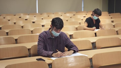 College students wearing face masks attend lecture at the University. Social Distancing measures and empty classroom due to Coronavirus Pandemic