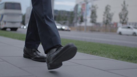 Close up of businessman legs walking down the street. Steps of a confident man in suit on a sidewalk in fast-paced city.