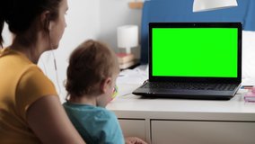 Woman in headphones with child sits at desk in bedroom, she looks at laptop green screen and talks to someone over Internet video connection, often nods her head approvingly. Close-up