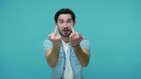 Aggressive irritated bearded guy in jeans shirt showing middle fingers at camera, offensive gesture of disrespect and hate, impolite rude expression. indoor studio shot isolated on blue background
