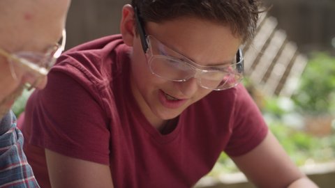 Close-up of a father and son wearing safety goggles going over plans and measurements for a backyard DIY project