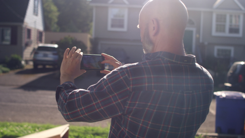 A father records his son ramping off a ramp with a skateboard on his smartphone camera