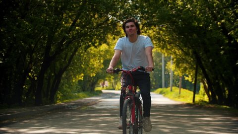 Young smiling happy man in white shirt riding a bike
