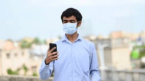 A man wearing face mask is making a video call on smartphone while being at terrace on home quarantine during pandemic of Coronavirus, covid-19 outbreak. 