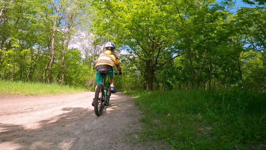 A boy rides a bicycle on a path in the forest. The road in the spring park.