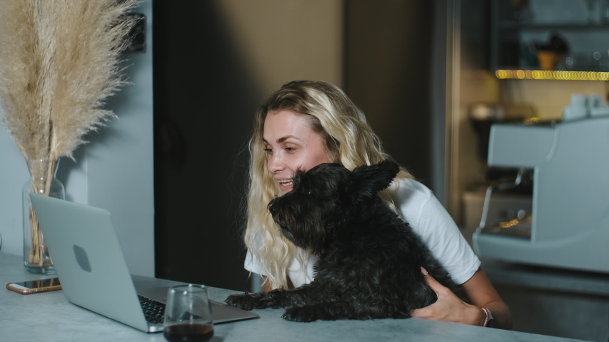 Happy smiling blonde woman waves her hand and makes a video call with friends on the computer. Female owner hugging adorable puppy dog and chatting at laptop camera with parents from home.
 | Shutterstock HD Video #1054252625
