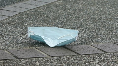 Slow motion of medical face mask fly with the wind on the floor in street. Lost disposable face mask for protection the coronavirus Covid-19.