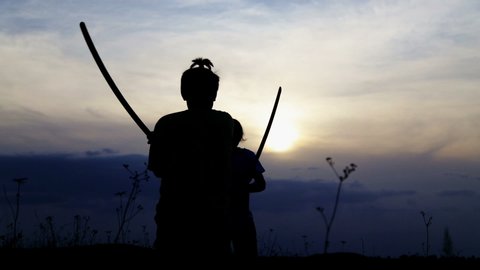 Teenage boys fencing with samurai training swords. Silhouette of exercising children in a field with swords.