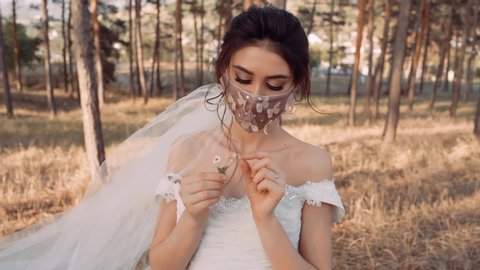 A portrait of a young woman dressed in a wedding dress. On her face she has a beautiful mask that fits her well. In her hand she has some Romanian flowers.