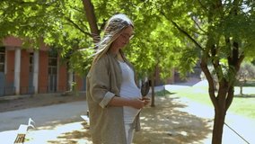 Young modern pregnant girl smiles at the camera on a sunny day, slow motion video, pregnant young girl