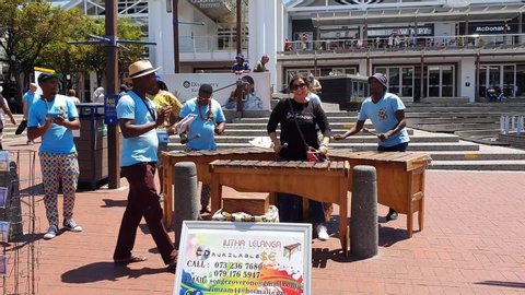 Cape Town, South Africa. January 28,  2020. Street musicians having fun with tourists on the waterfront area of central Cape Town. Woman interacts with band. Victoria & Alfred Waterfront with sound
