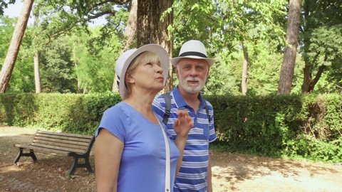 Front view of senior couple tourists walking along track in summer park Villa Borghese in Rome, Italy. Active modern life after retirement. Happy family enjoying time together in green garden
