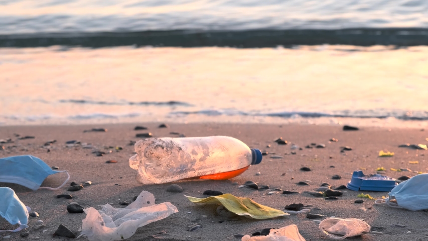 Disposable face masks and plastic debris on the beach in surf zone. Coronavirus COVID-19 is contributing to pollution, as discarded used masks clutter polluting urban beaches along with plastic trash | Shutterstock HD Video #1054261361