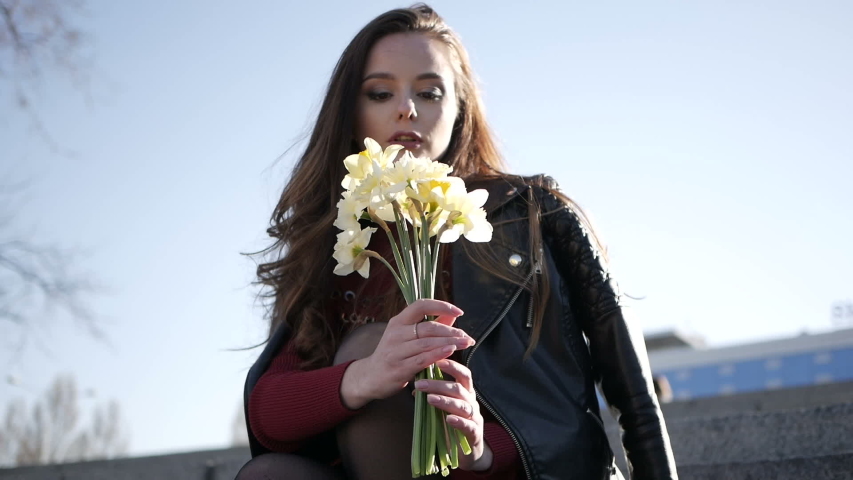 A young woman with a bouquet sits on the stairs in the park.