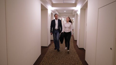 Man and woman walk by hotel corridor after meeting, smart casual clothes style. Young adult professionals return to rooms after successful meeting or conference