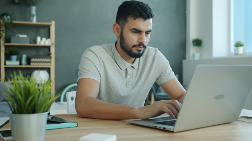 Unhappy Middle Eastern man is working with laptop at home then hitting table and leaving feeling stressed and failed. Workplace, technology and negative emotions concept. | Shutterstock HD Video #1054265072
