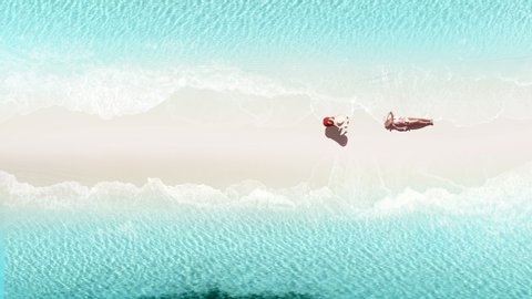 Aerial view of sea and white sand beach. Water surface texture, Top view ocean waves slow motion. Beautiful woman in bikini on tropical beach sand in summer.Aerial view of  Young girl lying on a beach