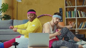 Goofy retro multi-ethnic men eating pizza, enjoying junk food, relaxing on sport mats and using laptop watching videos online training. Sports and humor. Fun concept.