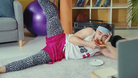 Retro stylish young man jerk eating pizza while doing leg exercises and watching training classes on laptop online. Fitness comedy. Sports and humor concept.