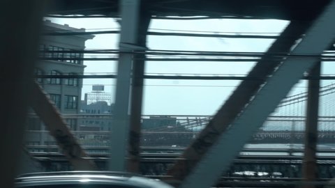 Looking out the window of a New York City subway train in motion (Brooklyn to Manhattan) going over the Manhattan Bridge with the Brooklyn Bridge in the background. Cinematic, hand-held POV shot.