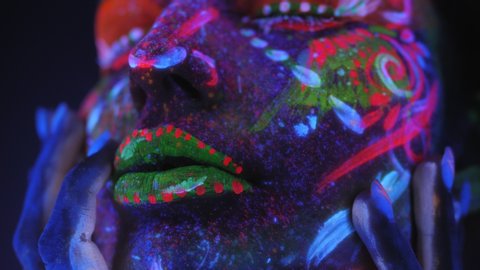 Close-up portrait of girl with a UV pattern on her face, on the eyes and lips bright multi colored makeup. Graceful model posing with UV pattern on body. Body art glowing in ultraviolet light.