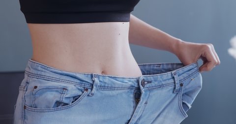 Successful weight loss. Young woman wearing too big jeans at home