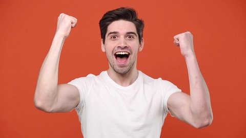 Young fun excited guy 20s 30s in white t-shirt isolated over orange background studio. People emotions lifestyle concept Looking camera doing winner gesture say Yes expressive gesticulating with hands